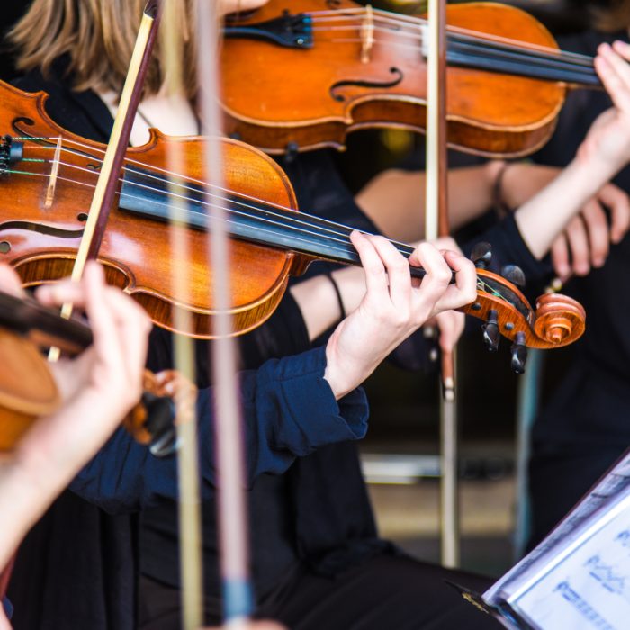 Violinspillere optræder live ved Symphony Sounds koncert, nærbillede af hænder og violiner.